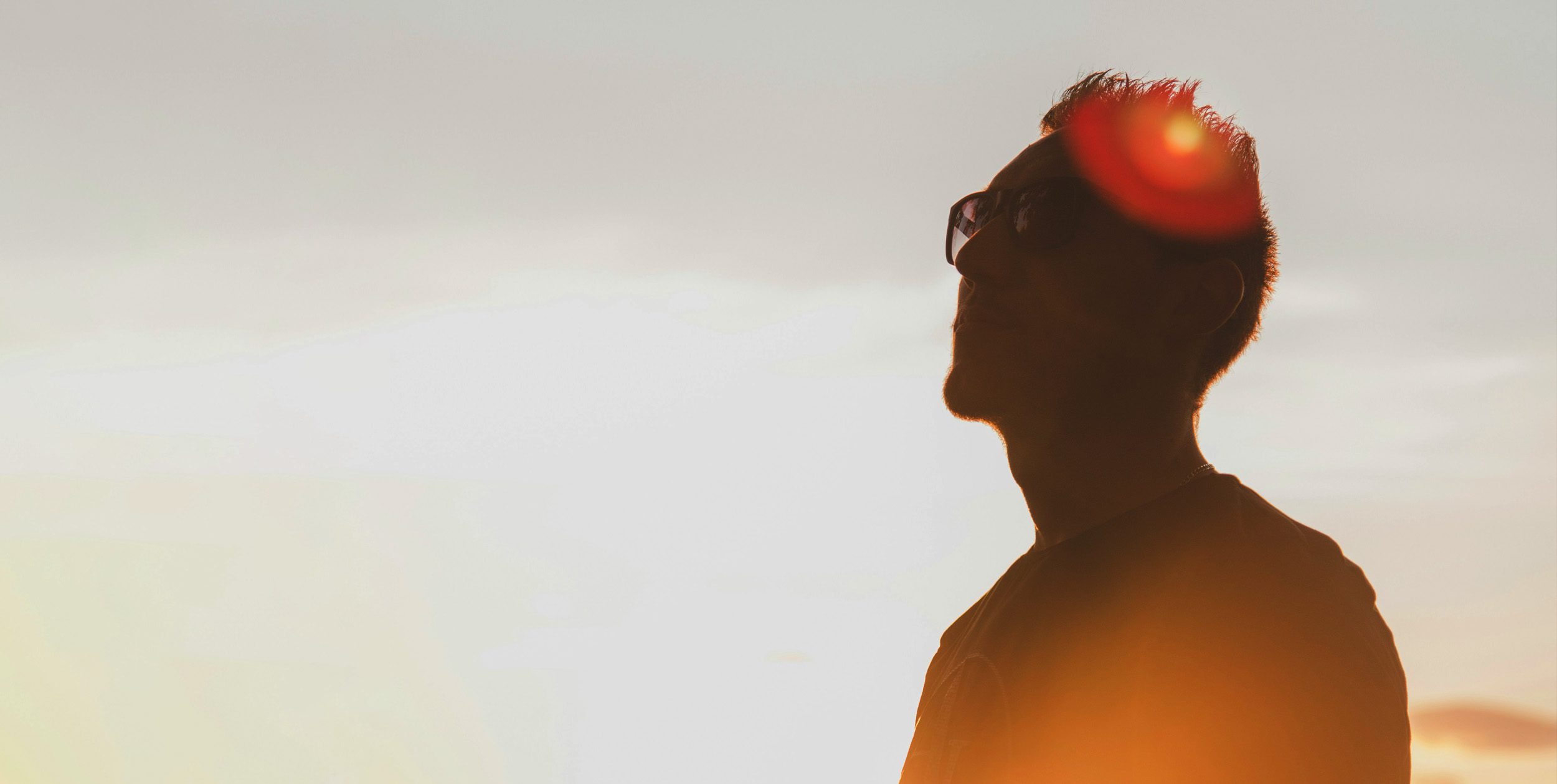 Ung man med solglasögon med skugga över ansiktet. Han ser sammanbiten ut och tittar uppåt.