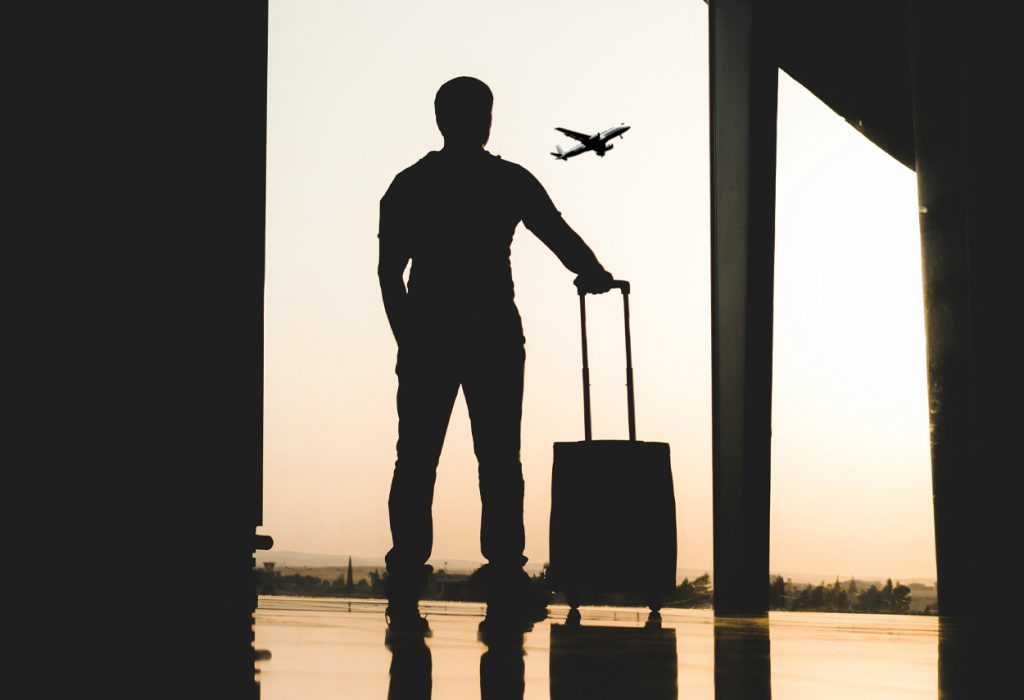 Man på flygplats står vid ett fönster och ser ett flygplan lyfta mot himlen.